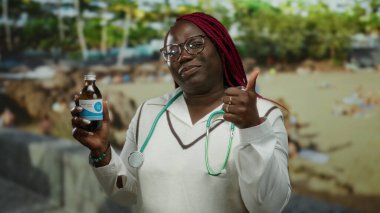 Deniz kenarındaki plajda elinde ilaç steteskobu tutan kadın gülümseyen Afro-Amerikan açık hava tıbbi, canlı, profesyonel arka plan.