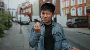 Etkileyici jestleri olan genç bir adam canlı bir şehir caddesinde duruyor, canlı şehir ortamını yakalıyor..