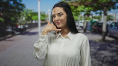 Güneşli bir sokak sahnesinde neşeli bir ifadeyle beni işaret eden bir kadın, gençlik enerjisini yakalıyor ve canlı bir şehir ortamında davetkar bir tavır sergiliyor..