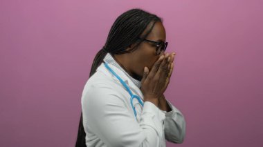 Gözlüklü ve steteskop takan doktor pembe bir duvara dayanıyor, odaklanmış ve sıcak görünüyor, sağlık ve modern estetiğin kesişimlerini genç bir varlıkla vurguluyor..