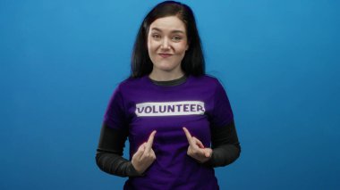 Mor gönüllü gömlekli bir kadın mavi arka planda kameraya doğru hareketli bir şekilde gülümsüyor, coşkuyu ve toplumsal bağlılığı somutlaştırıyor..