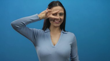 Genç İspanyol kadın gülümsüyor ve mavi uzun kollu gömleğiyle, gözleri kapalı, canlı mavi duvarlara karşı barış işareti yapıyor..
