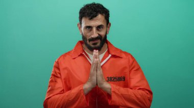 Turuncu hapishane tulumlu İspanyol sakallı adam yeşil bir geçmişe karşı dua ediyor. Hapis içinde umut ve iç gözlem taşıyor..