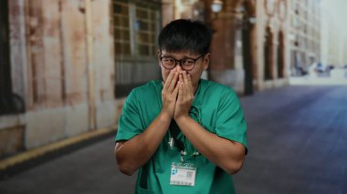 Yeşil önlüklü genç bir adam bir şehir sokağında gün içinde şaşkın bir şekilde dikiliyor..