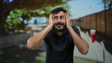 Sakallı İspanyol bir adam, güneşli bir çevrede sokakta hayal kırıklığına uğramış görünüyor..