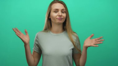 Canlı yeşil bir arka plan duvarının üzerinde kendinden emin bir ifadeyle omuz silken bir kadın, belirsizlik ya da kayıtsızlık ifade ediyor, izole ve sıradan bir gömlek içinde..