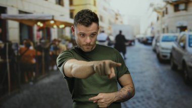 Yeşil tişörtlü bir adam canlı şehir caddesini gösteren dövmeli bulanık insanlar ve arka planda odak ve açık havada etkileşim gösteren araçlar..