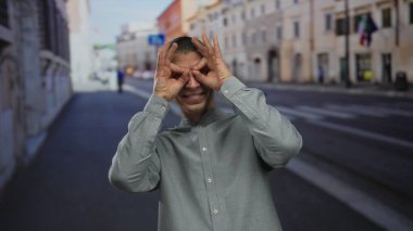 Kafkasyalı bir adam sokakta elleri ile el kol hareketi yapıyor, gri gömlek giyiyor, bulanık şehir geçmişiyle dışarıda duruyor, gün ışığında eğlence ve yaratıcılığını ifade ediyor..