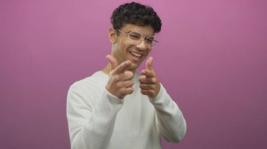Pembe stüdyo ortamında gülümseyen ve işaret parmağıyla işaret eden bir adam..