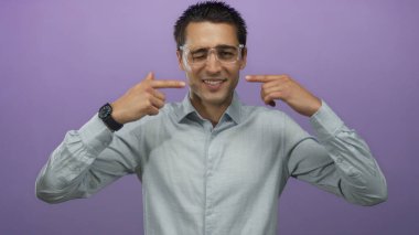 Gözlüklü genç İspanyol adam gülümseyip kendine doğru hareketler yapıyor. Canlı mor bir arka plan, günlük kıyafetleri ve olumlu ifadesiyle münzevi bir portre yaratıyor.