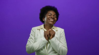 Beyaz takım elbiseli bir kadın canlı mor bir arka plana gülümsüyor, mutluluk ve profesyonellik sergiliyor, ellerini canlı bir şekilde kaldırıyor..