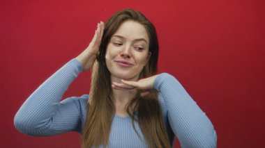 Kadın yüzü güzel ışıklandırılmış bir stüdyoda elleri ile canlı kırmızı bir duvara karşı, nazikçe gülümsüyor;.