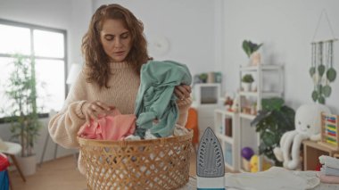Kadın, sepetler ve bitkilerle çevrili, sıcak, aydınlık bir çamaşırhanede giysileri katlıyor, günlük ev rutinlerini ve rahat bir ev ortamını somutlaştırıyor..
