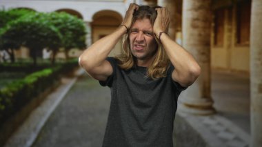 Erkek, binadaki uzun sarı saçları hem gerilmiş kolları hem de büzüşmüş dudakları, yukarı bakan gözleri, stresi kavrar..