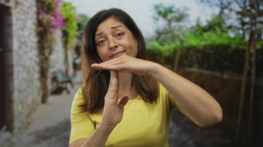 Kadın, şehir caddesinde ellerinin begonville ve taş duvarla kaplı olduğu bir yerde gün ışığında jest yapıyor; tefekküre ara verin..