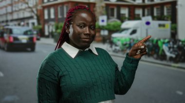 Şehir caddesinde gülümseyen bir kadın yeşil süveter ve örgü takmış neşeli bir ifade ve canlı bir çevre sergiliyor..