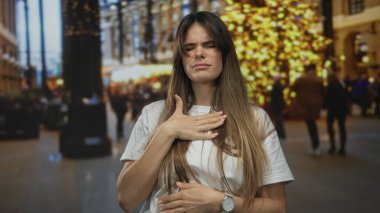 Genç bir kadın, kalabalık arka planı bulanık ve yoğun ışıklarla dolu, keyifli bir şehir sokağında kendini kötü hissediyor. Rahatsızlık ve stresi ifade ediyor..