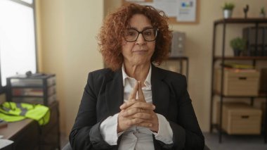 Ofis ortamında düşünen, gözlüklü ve takım elbiseli, düşünceli bir ifadeyle düşünceli bir kadın, içeride düşüncenin ve profesyonelliğin özünü vurguluyor..