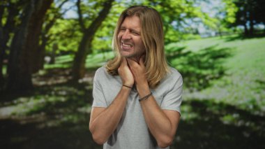 Sarışın adam, ormanın ortasındaki güneş ışığının filtrelenmiş gölgesinde boğaz tutar; gerginlik gerginliği gerer..