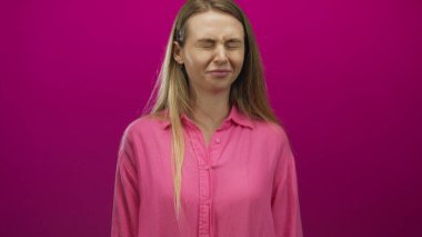 Pembe gömlekli, gözleri kapalı bir kadın izole edilmiş pembe bir arka plana karşı duruyor. Stres ve tefekkür duyguları yayıyor..