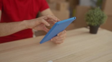 Genç adam bir eliyle mavi tableti tıklatırken diğer eliyle ahşap masaya vuruyor..