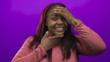 Mor stüdyoda elleri yanaklarında gülen Afro-Amerikalı kadın pembe bluz giyiyor. Sürpriz bir keşif..