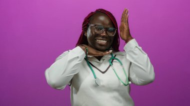 Gülümseyen Afro-Amerikan kadın doktor steteskopla canlı pembe bir arka plana karşı şakacı poz veriyor, kendine güven ve neşe saçıyor..