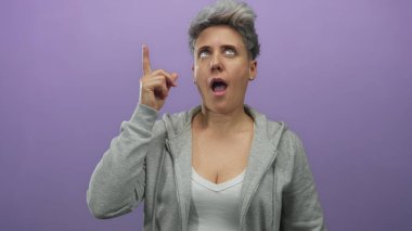 Kadın parmağını yukarı kaldırır ve gözleri stüdyoda mor arka planda ayrık dudaklarla kapatır; kendine güven.