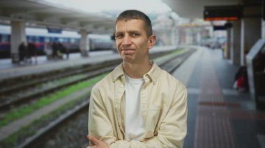 Bulanık tren rayları ve arka planda yolcularla dolu yoğun bir tren istasyonunda güvenle duran adam, kentsel seyahat ve ulaşım temalarını gözler önüne seriyor..