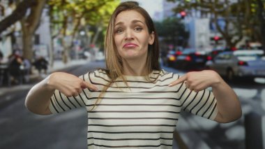 Yoğun şehir caddesinde arka planda bulanık trafiği olan çizgili gömleği gösteren beyaz bir kadın. Sürpriz..