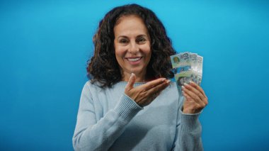 Gülümseyen kadın, Avustralya dolarlarını tutuyor. Mavi duvara başparmak işareti yapıyor. Finansal başarı fikrini gösteriyor..