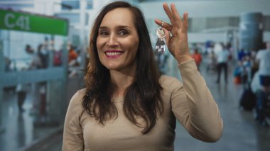 Havaalanının yoğun terminalinde elinde anahtarlarla gülümseyen bir kadın neşeli seyahat duyguları yakalıyor.