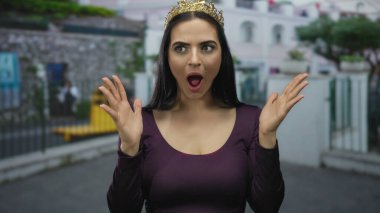 Tacını takan genç İspanyol kadın, sokak ortasında şaşkınlığını dile getiriyor. Sokak arkaplanına karşı elleri havada, duygu ve güzellik gösterisi yapıyor.
