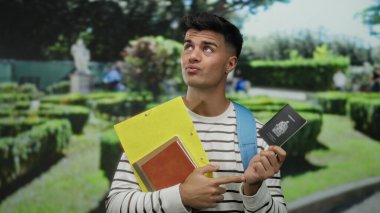 Adam, Kanada pasaportu ve belgelerini bir parkta tutuyor. Üzerinde çizgili gömlek ve mavi bir sırt çantası var. Pasaportu düşünceli bir ifadeyle işaret ediyor..