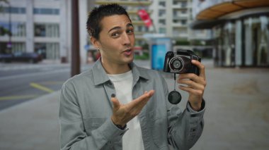 Genç İspanyol asıllı bir adam, şehir caddesindeki kameraları merakla inceliyor. Etrafı uzun ve modern binalarla çevrili. Teknoloji ve metropoliten yaşamın ilginç bir karışımını sergiliyor..