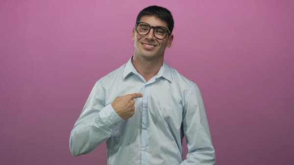 Мужчина в очках в светло-голубой рубашке улыбается и тычет пальцем в грудь о розовую стену студии; уверенность.