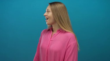 Pembe gömlekli bir kadın izole edilmiş mavi bir arka plan duvarına gülümsüyor, gençlik enerjisini ve pozitifliği canlı bir ortamda yakalıyor..