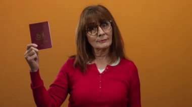 Turuncu duvara karşı Filipinli pasaportu tutan son sınıf öğrencisi kadın, izole edilmiş arka planda seyahat kavramını ifade ediyor..