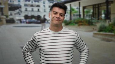 Striptiz tişörtlü genç adam şehir sokaklarında komik jestler yapıyor modern mimari arka planda şakacı davranışlar sergiliyor açık hava kentsel çevre portresi yakışıklı.