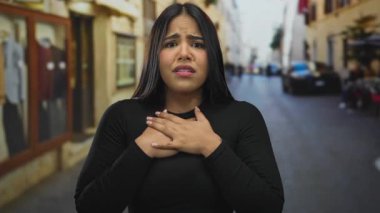 Yoğun bir caddede, göğsü göğsünde endişeli görünen bir kadın, şehir ortamında duygularını ifade ediyor..