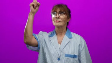 İspanyol temizlikçi kıdemli kadın canlı pembe bir duvarın önünde duruyor, kendine güvenerek gülümsüyor ve çeşitli pozlarda başparmak işareti yapıyor..