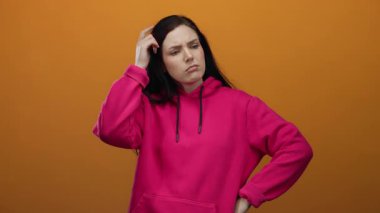 Turuncu arka plana pembe kapüşonlu bir kapüşon takan bir kadın derin düşüncelerini düşünceli bir yüz ifadesiyle ifade ediyor..