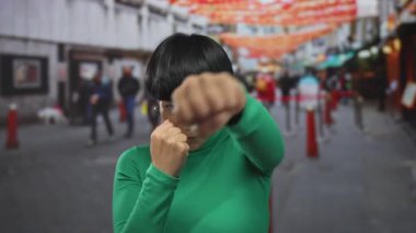 Genç Çinli kadın renkli fenerlerle süslenmiş canlı bir şehir caddesinde boks yapıyor. Enerji ve şehir kültürünü somutlaştırıyor..