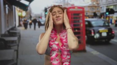 Bikinili genç sarışın kadın telefon kulübesinin dışında elleri ile yüzünü tutuyor; stres bunalımı.