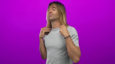 Sarışın adam, stüdyo ortamında kamera lensine bakarken uzun saçlarını ayarlıyor..