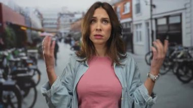 Çevresi bisiklet ve şehir manzarasıyla çevrili, hareketli bir şehir sokağında hareketli genç İspanyol kadın, açık havada günlük giysiler ve kol saati giyiyor..