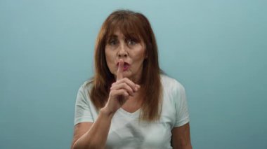 Mavi duvara parmak atarak sessizce el kol hareketi yapan, beyaz gömlek giyen, mahremiyetini ifade eden, minimalist ortamda tecrit edilmiş yaşlı İspanyol kadına odaklanan bir kadın..