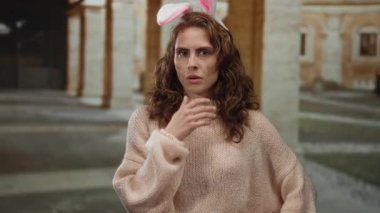 Tavşan kulağı takan bir kadın eski bir üniversitede düşünceli görünüyor. Tarafsız bir ifadeyle iç mekanlara yerleşiyor, ilginç ve düşünceli bir atmosfer sergiliyor..