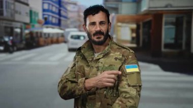 Ukrayna bayraklı askeri üniformalı bir adam açık bir şehir caddesinde güvenle duruyor..