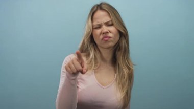 Ciddi ifadeleri olan sarışın kadın mavi stüdyoyu işaret ediyor; suçlama onaylanmamış eleştiri.